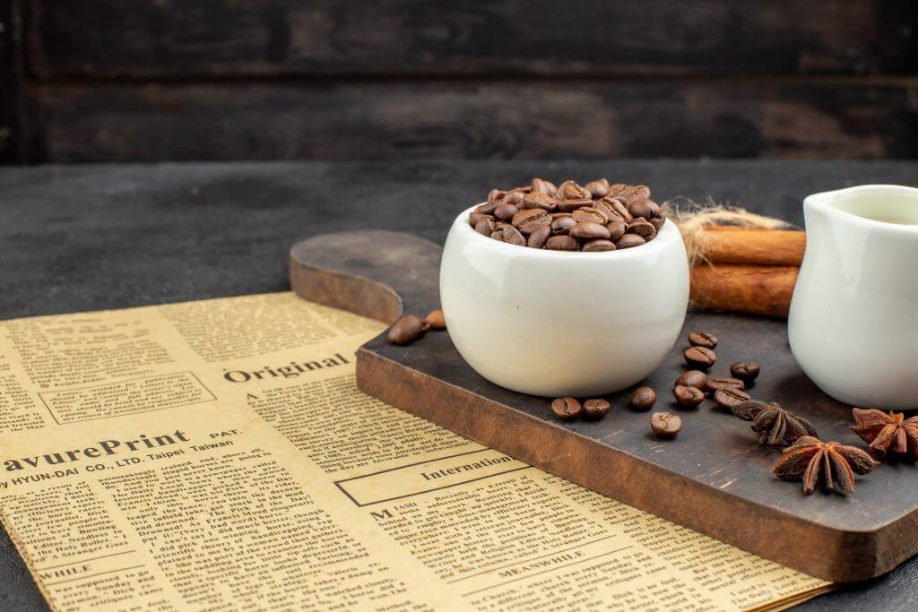 bottom view roasted coffee beans bowl anises cinnamon sticks small milk bowl wood board dark 1