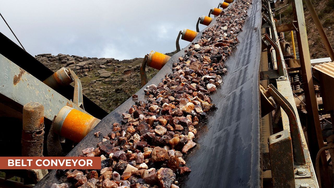 Close-up of a belt conveyor system carrying small rocks or minerals, with rollers supporting the conveyor belt in an industrial mining environment