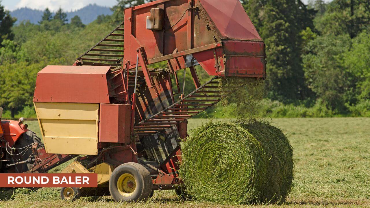 A red and yellow round baler attached to a tractor producing a tightly rolled bale of hay in a green field surrounded by trees on a sunny day