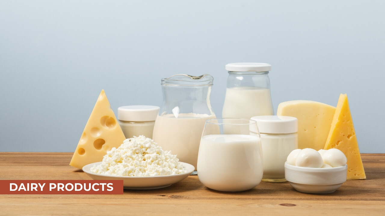 A variety of dairy products displayed on a wooden table including milk, cheese, yogurt, and fresh mozzarella, with a light blue background